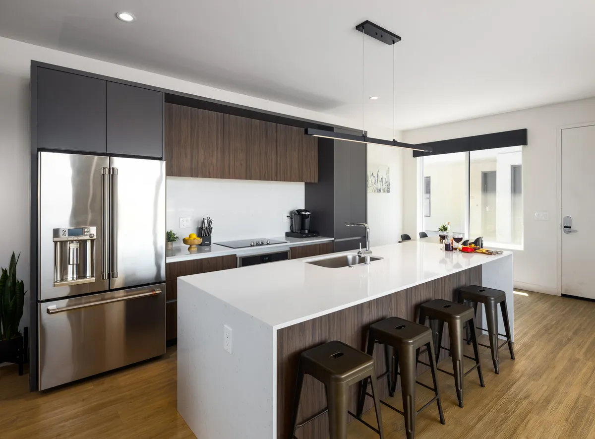 A contemporary kitchen featuring an expansive island with bar stools, stainless steel Caf appliances, and dark cabinetry. The open layout encourages socializing and cooking, with ample space for guests to gather around and enjoy appetizers or drinks.