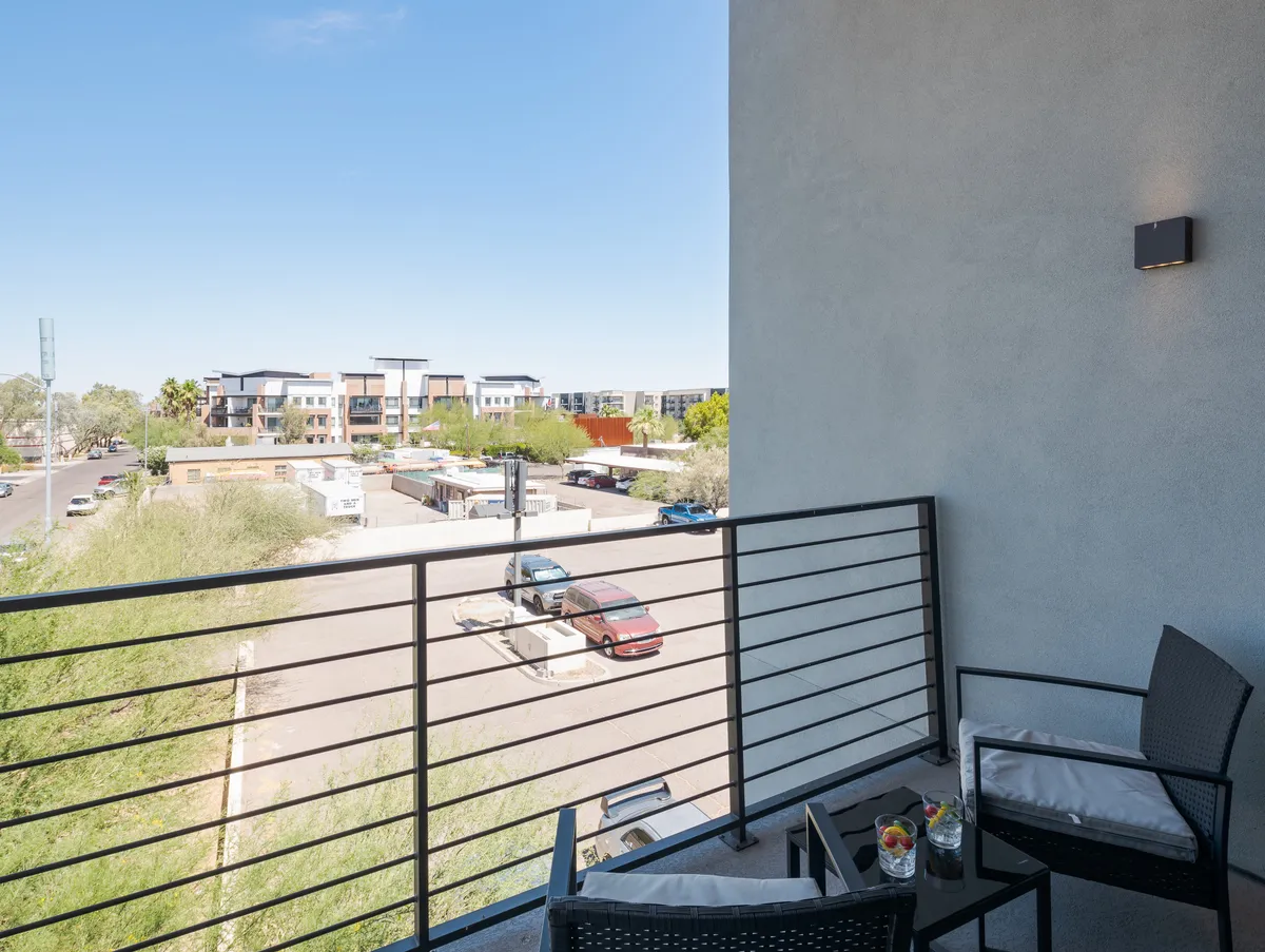 Another angle of a balcony space, this time featuring cozy seating and a decorative table set against an urban backdrop. The ambiance is relaxed, highlighting opportunities to unwind after a busy day while still being connected to the city’s energy.