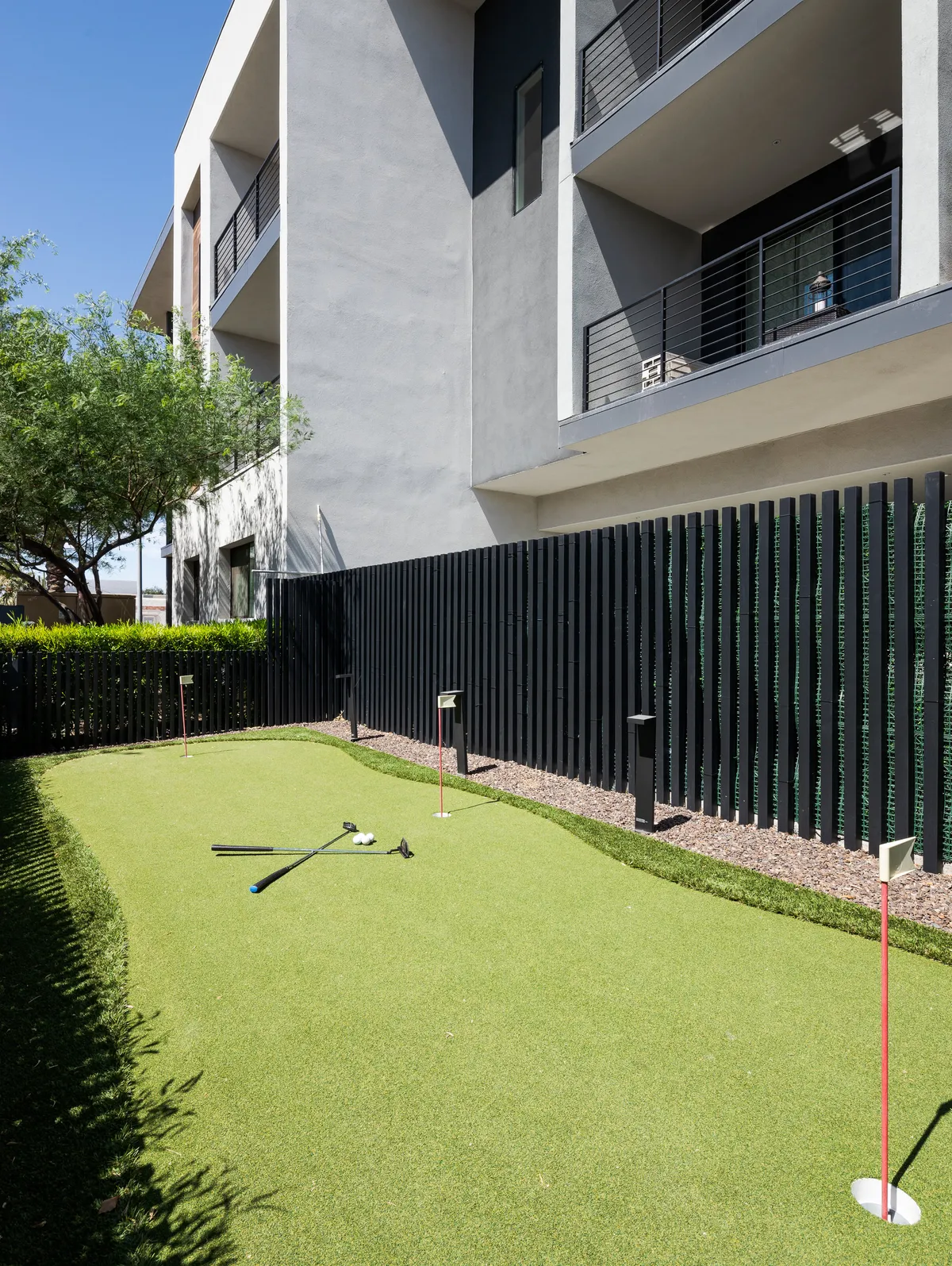 A playful exterior scene showcasing a manicured putting green with golf clubs at the ready and fencing in the background. The area is bathed in sunlight, inviting friendly competition and casual relaxation.