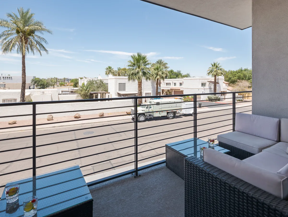 A private balcony with comfortable seating, palm trees swaying in the background, and a view over the street below. The space is perfect for relaxing with a drink, enjoying warm evenings, or watching the sunset.