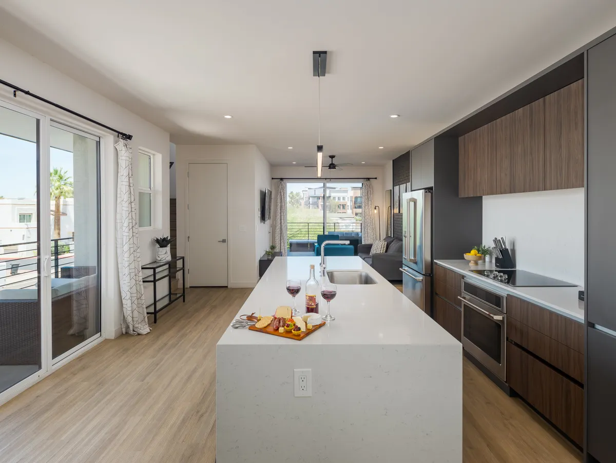 A bright, contemporary kitchen with a prominent island, wine glasses, a snack platter, and expansive windows letting in natural light. The modern design is clean yet welcoming, suggesting a high standard of comfort and hospitality.