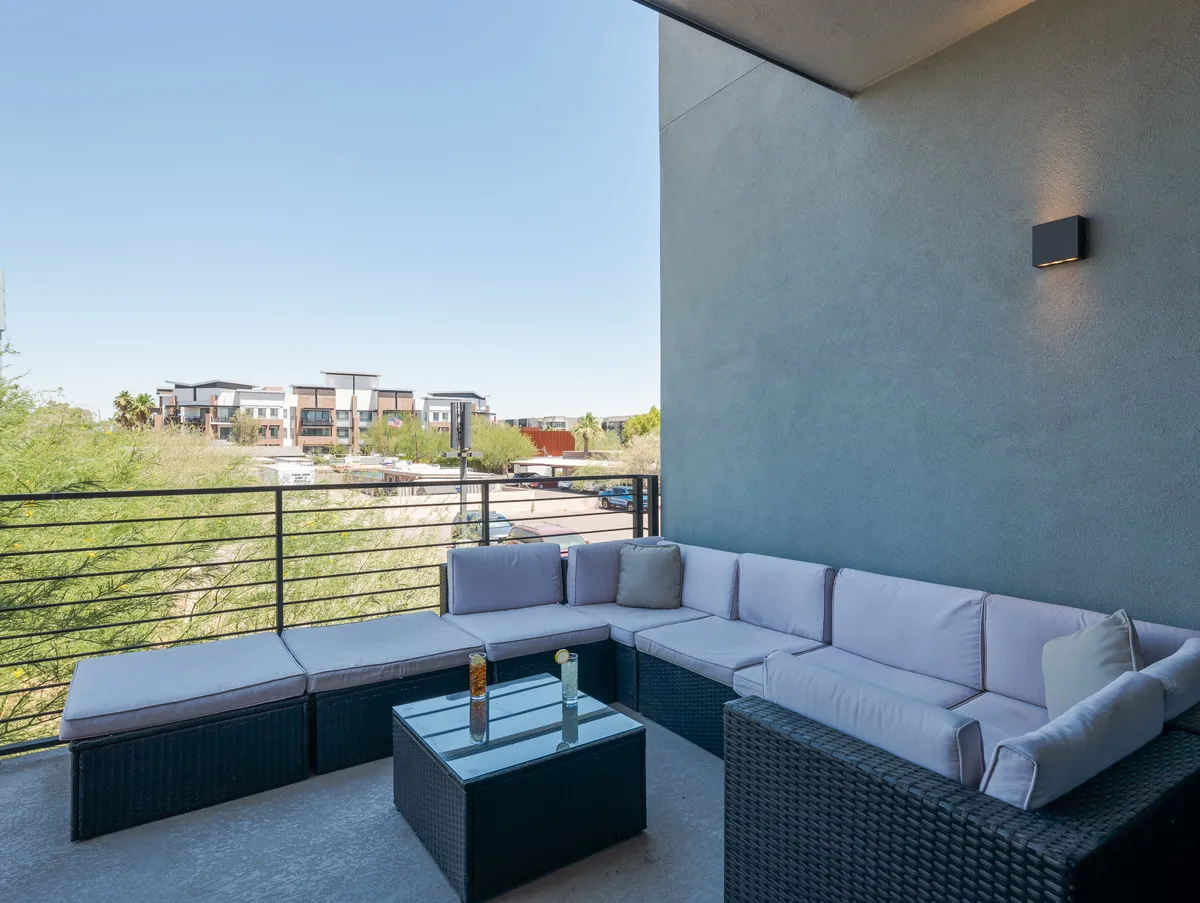 The image showcases a stylish balcony lounge area with a modern modular sectional sofa and a sleek glass coffee table, set against a backdrop of city views. The space invites relaxation and social gatherings, with ample seating and a picturesque spot to watch the sunset or enjoy drinks with friends.